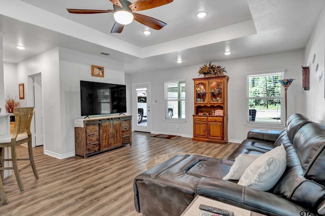 living room featuring wood-type flooring, a raised ceiling, and ceiling fan