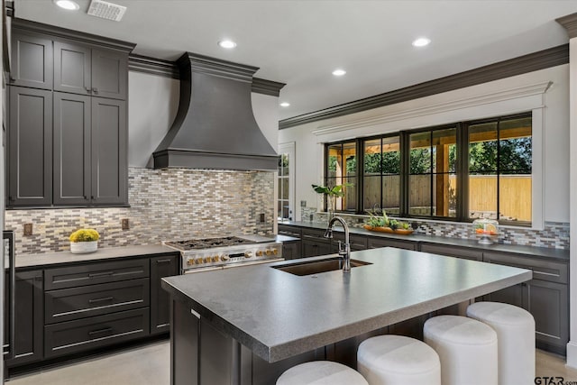 kitchen featuring a breakfast bar, double oven range, sink, an island with sink, and custom range hood