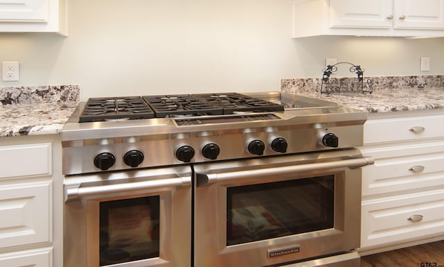 interior details featuring white cabinets, double oven range, and light stone countertops