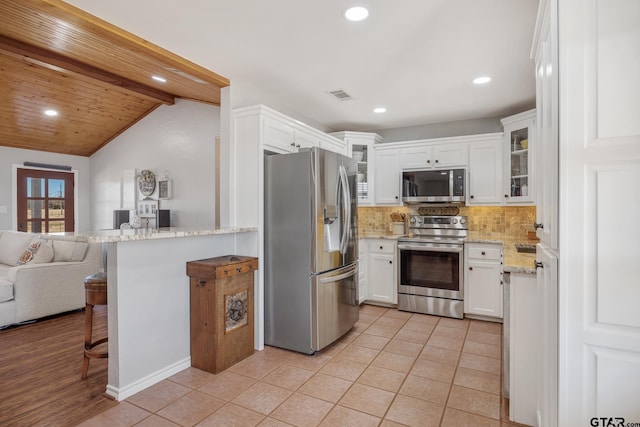 kitchen with a kitchen bar, white cabinetry, light stone counters, stainless steel appliances, and decorative backsplash