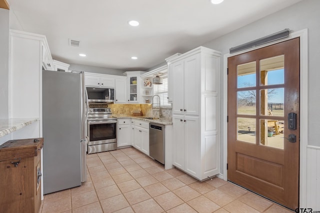 kitchen featuring sink, white cabinetry, stainless steel appliances, light stone counters, and decorative backsplash