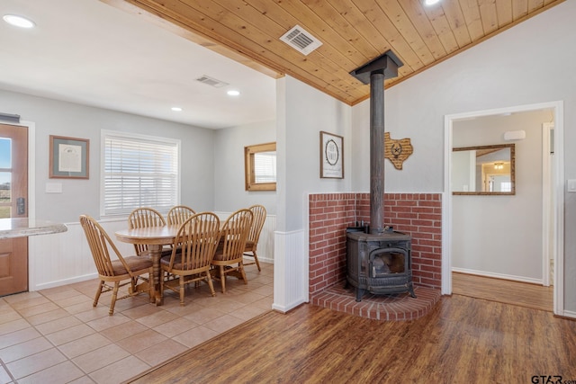 dining space with vaulted ceiling, wooden ceiling, light hardwood / wood-style floors, and a wood stove