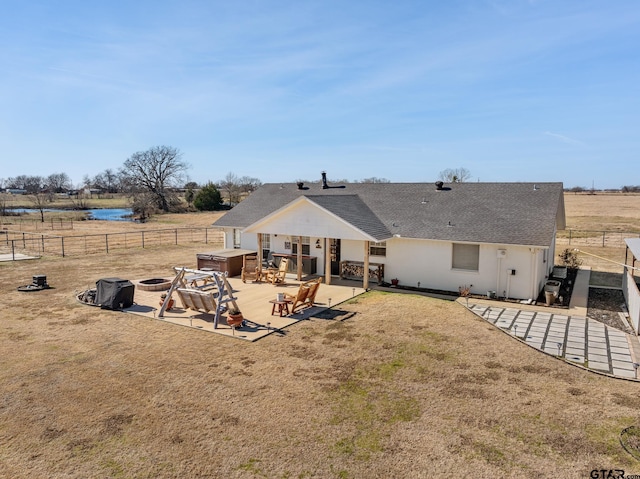 back of house featuring a lawn, a jacuzzi, an outdoor fire pit, a rural view, and a patio area