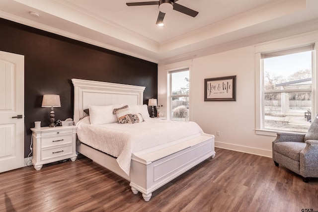 bedroom with ornamental molding, a tray ceiling, dark wood-style flooring, and baseboards