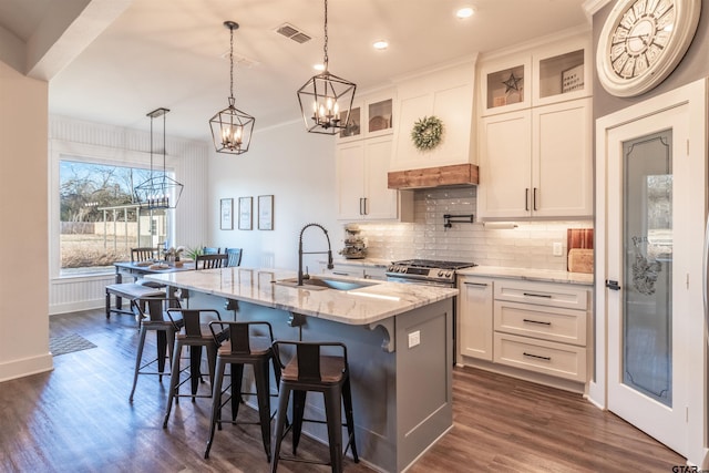 kitchen with visible vents, light stone counters, a kitchen island with sink, white cabinetry, and a sink