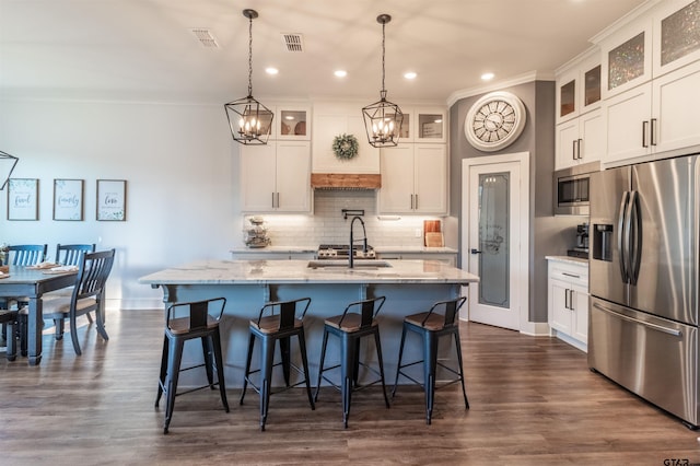 kitchen with visible vents, appliances with stainless steel finishes, a sink, a kitchen island with sink, and backsplash