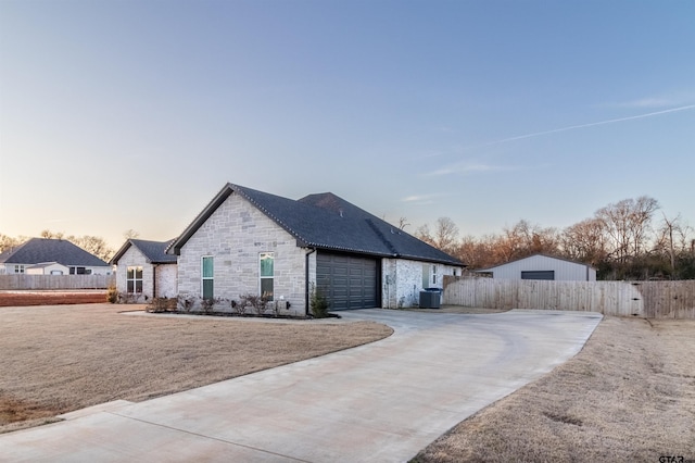 view of property exterior with an attached garage, central air condition unit, fence, stone siding, and driveway