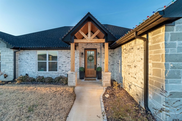 property entrance with a shingled roof and brick siding