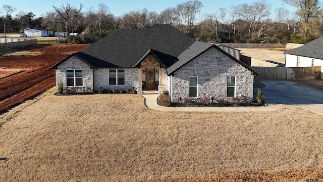 view of front facade with a front yard, stone siding, and fence