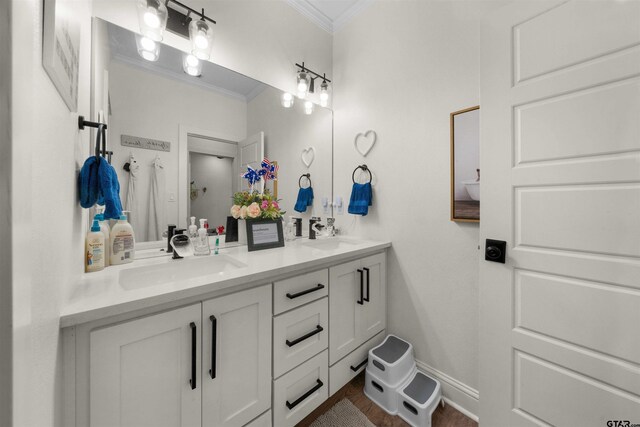 full bath with baseboards, double vanity, a sink, and crown molding