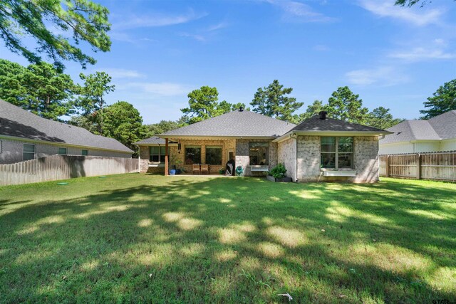 rear view of property with brick siding, a fenced backyard, roof with shingles, and a yard