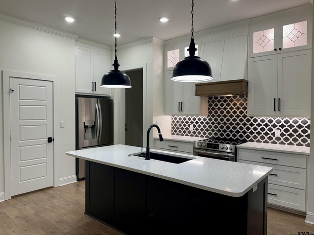 kitchen with appliances with stainless steel finishes, wood finished floors, a sink, light countertops, and backsplash