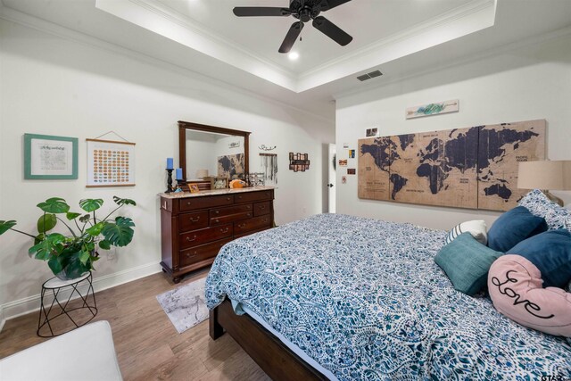 bedroom featuring baseboards, visible vents, ornamental molding, wood finished floors, and a tray ceiling