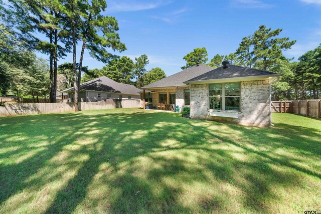 back of property featuring roof with shingles, brick siding, a yard, and fence