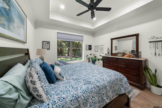 bedroom featuring recessed lighting, wood finished floors, a ceiling fan, a raised ceiling, and crown molding