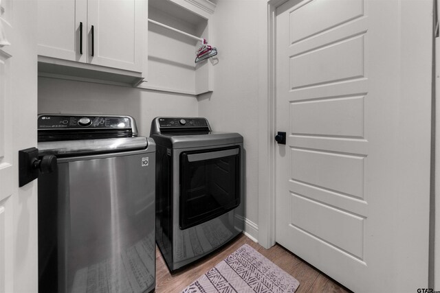 laundry room with cabinet space, washing machine and dryer, baseboards, and light wood-style floors