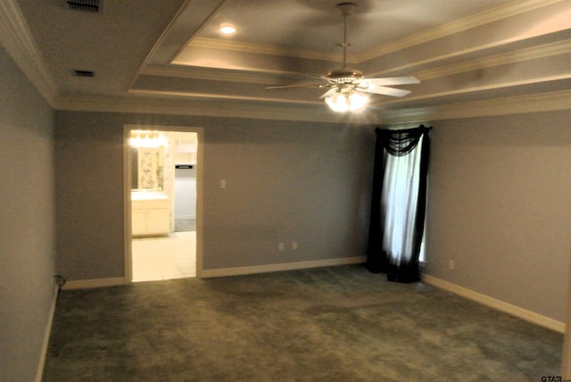 empty room with ceiling fan, dark colored carpet, a raised ceiling, and crown molding