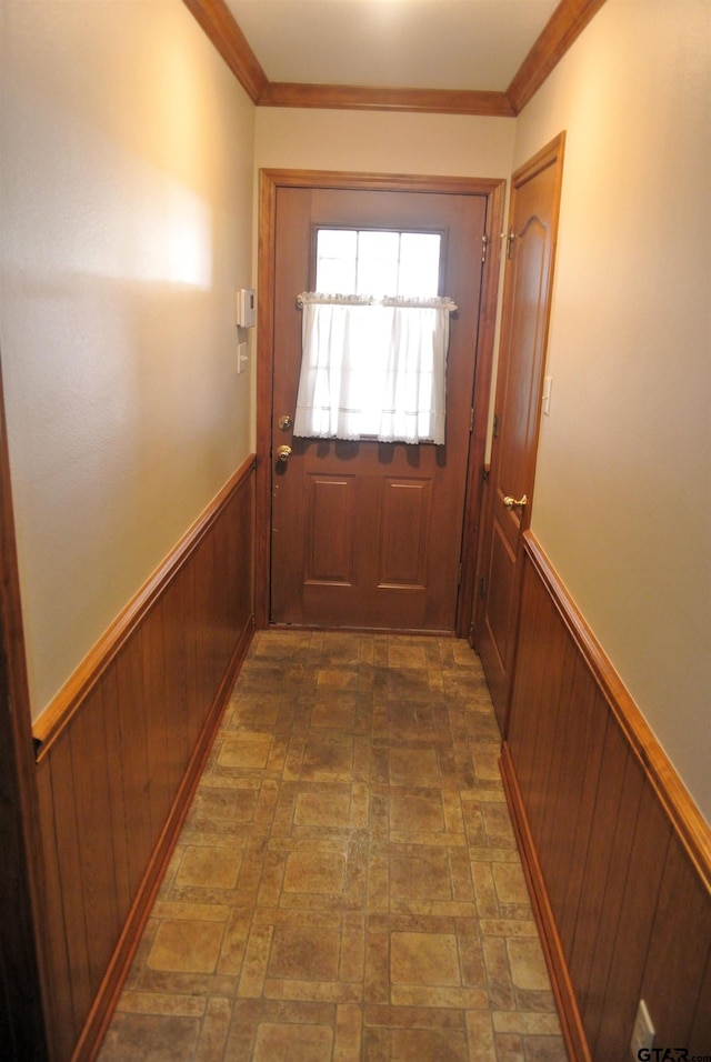 doorway with ornamental molding and wood walls