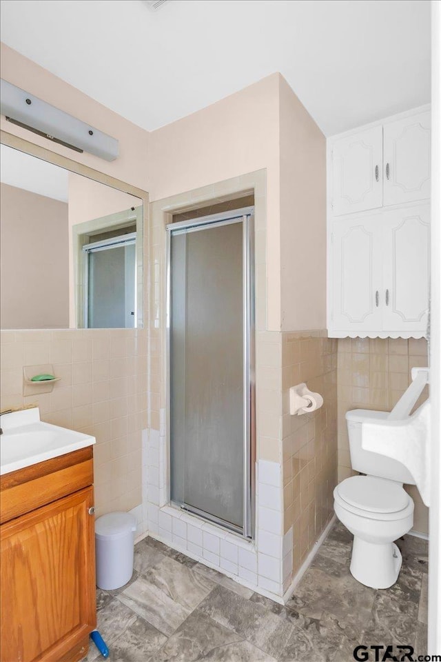 bathroom featuring tile walls, vanity, toilet, and a shower with door