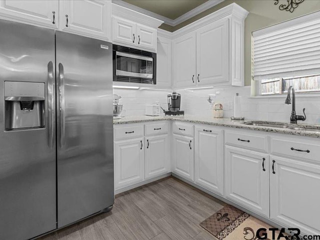 kitchen featuring white cabinets, appliances with stainless steel finishes, sink, light wood-type flooring, and light stone counters