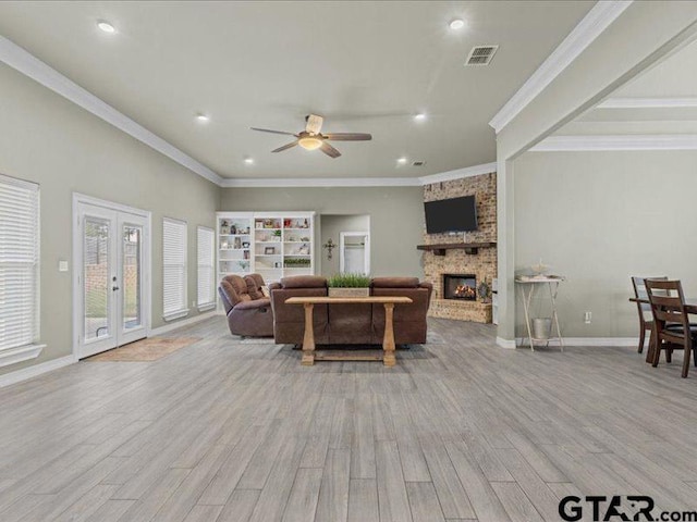 living room featuring french doors, a stone fireplace, light hardwood / wood-style floors, ceiling fan, and crown molding