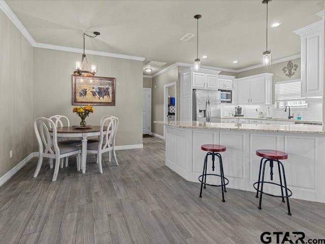 kitchen featuring light stone countertops, appliances with stainless steel finishes, white cabinetry, and pendant lighting