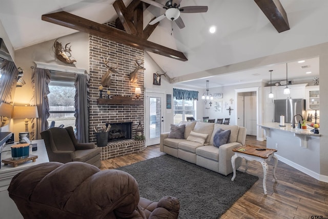 living room with dark wood-type flooring, ceiling fan, a brick fireplace, and vaulted ceiling with beams