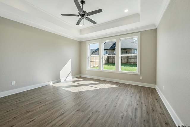 empty room with ceiling fan, wood-type flooring, ornamental molding, and a raised ceiling