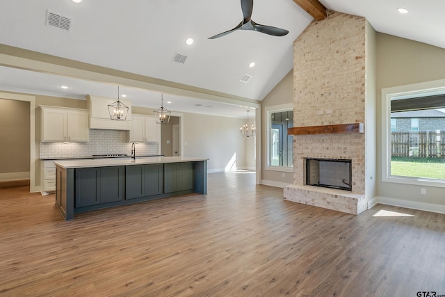 kitchen with pendant lighting, light hardwood / wood-style flooring, beam ceiling, and an island with sink