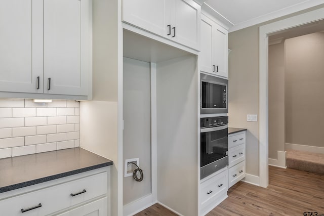 kitchen featuring appliances with stainless steel finishes, decorative backsplash, wood-type flooring, and white cabinets