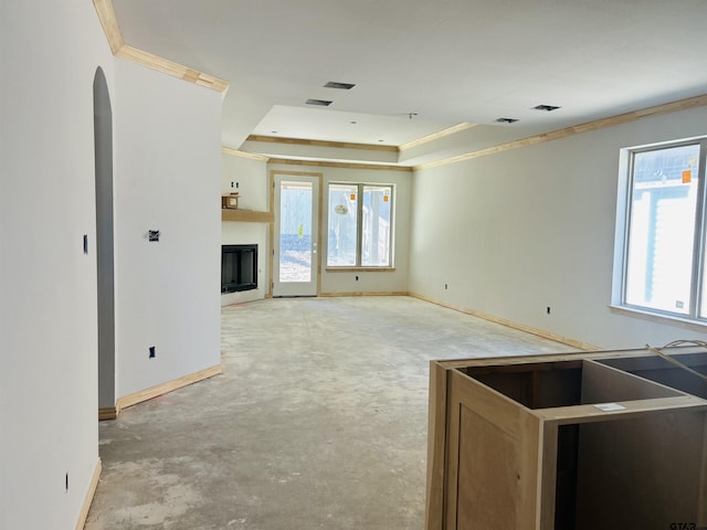 unfurnished living room with concrete floors, a fireplace, baseboards, a tray ceiling, and crown molding