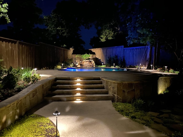pool at night featuring a fenced in pool, a fenced backyard, and a patio