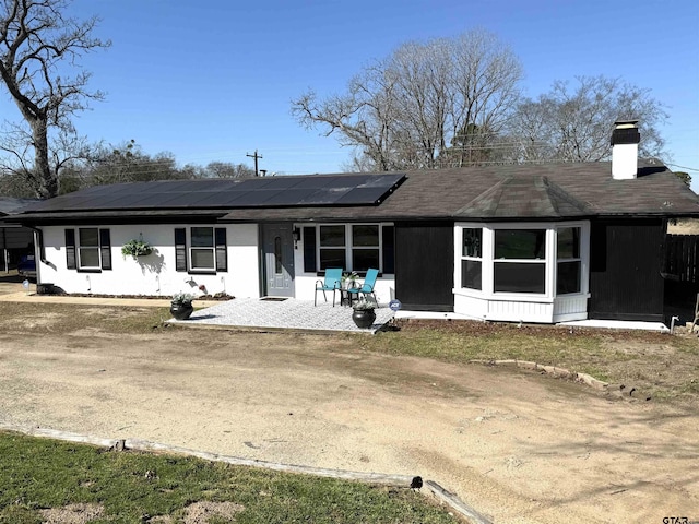 back of property featuring roof mounted solar panels, driveway, a chimney, and a patio