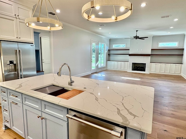 kitchen with hanging light fixtures, light stone countertops, light hardwood / wood-style flooring, and appliances with stainless steel finishes