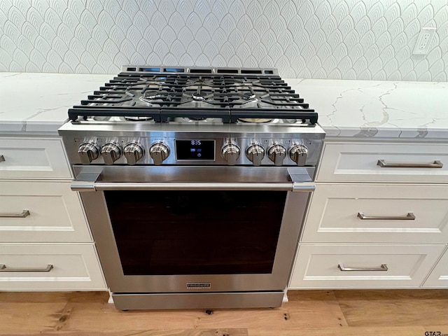 interior details with light stone countertops, stainless steel range, and white cabinets