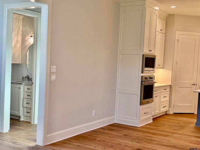 kitchen with white cabinets, stainless steel appliances, sink, and light hardwood / wood-style flooring