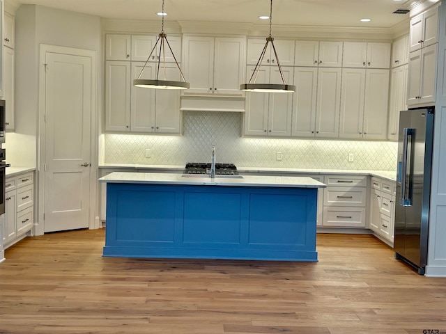 kitchen featuring high end refrigerator, decorative light fixtures, light hardwood / wood-style floors, and a kitchen island with sink