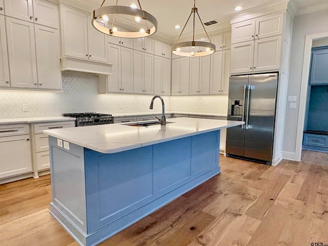 kitchen featuring light wood-type flooring, premium appliances, hanging light fixtures, sink, and an island with sink