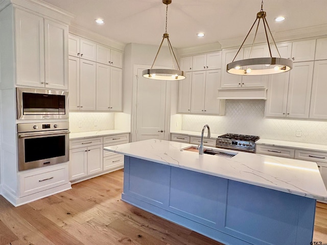 kitchen with a kitchen island with sink, appliances with stainless steel finishes, hanging light fixtures, white cabinets, and light hardwood / wood-style flooring