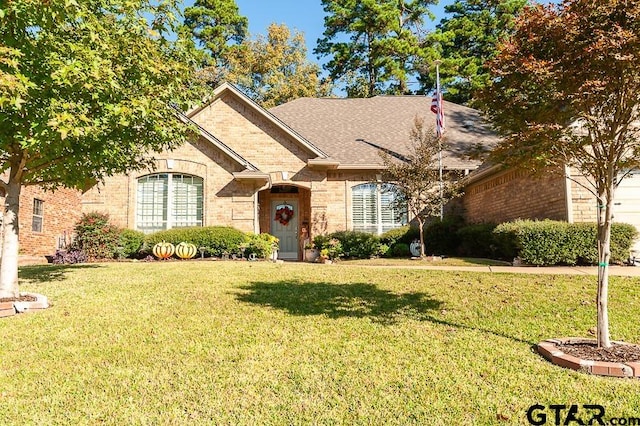 view of front of home with roof with shingles, a front lawn, and brick siding