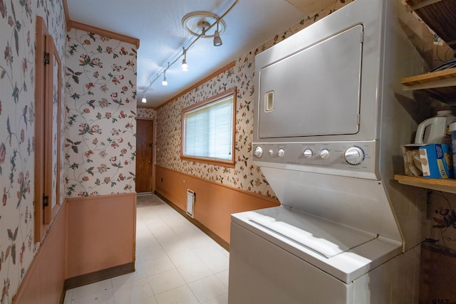 laundry room featuring stacked washing maching and dryer, rail lighting, and crown molding