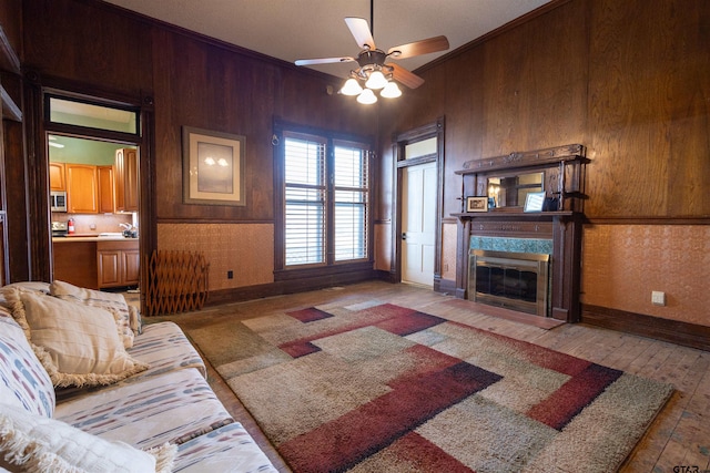 living room with wood walls, ceiling fan, a premium fireplace, wood-type flooring, and crown molding