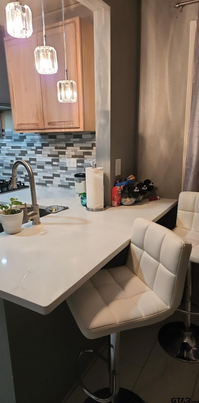 kitchen featuring pendant lighting, light brown cabinets, tasteful backsplash, and a breakfast bar area