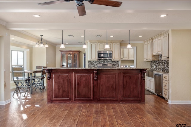 kitchen featuring light stone counters, a center island, hanging light fixtures, appliances with stainless steel finishes, and beam ceiling