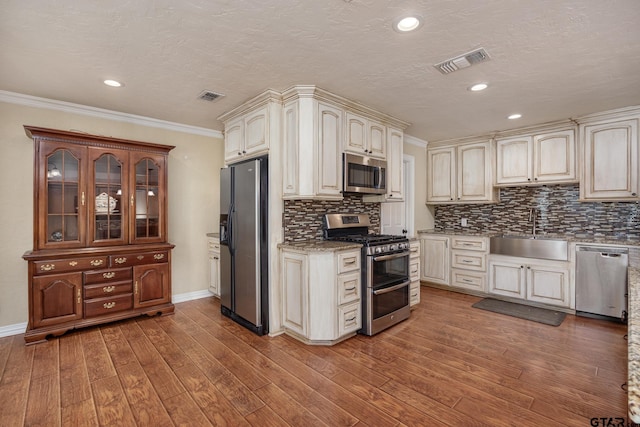 kitchen with sink, hardwood / wood-style flooring, ornamental molding, and stainless steel appliances