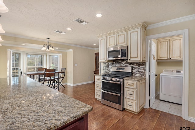 kitchen with crown molding, appliances with stainless steel finishes, light stone counters, washer / dryer, and decorative light fixtures