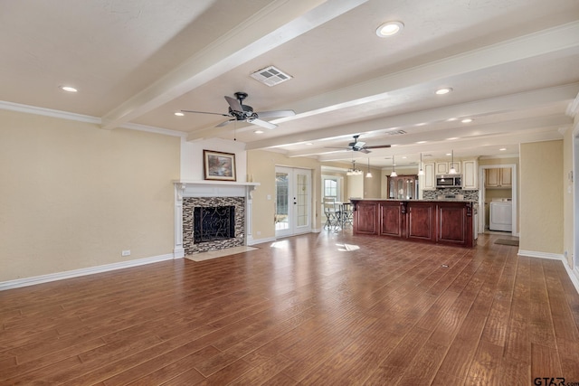 unfurnished living room featuring beamed ceiling, washer / clothes dryer, dark hardwood / wood-style flooring, a tiled fireplace, and ceiling fan