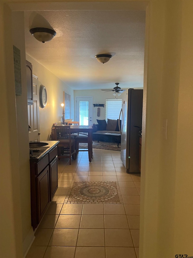 kitchen featuring ceiling fan, dark brown cabinets, stainless steel refrigerator, and light tile patterned flooring