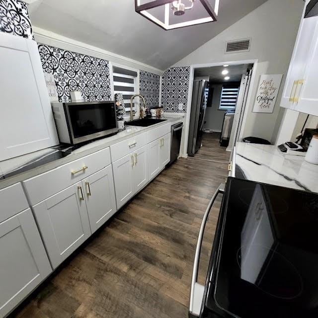 kitchen featuring stainless steel appliances, sink, lofted ceiling, white cabinets, and dark wood-type flooring