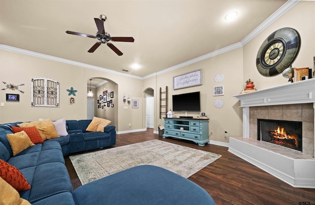 living room featuring ceiling fan, dark hardwood / wood-style floors, a tiled fireplace, and ornamental molding